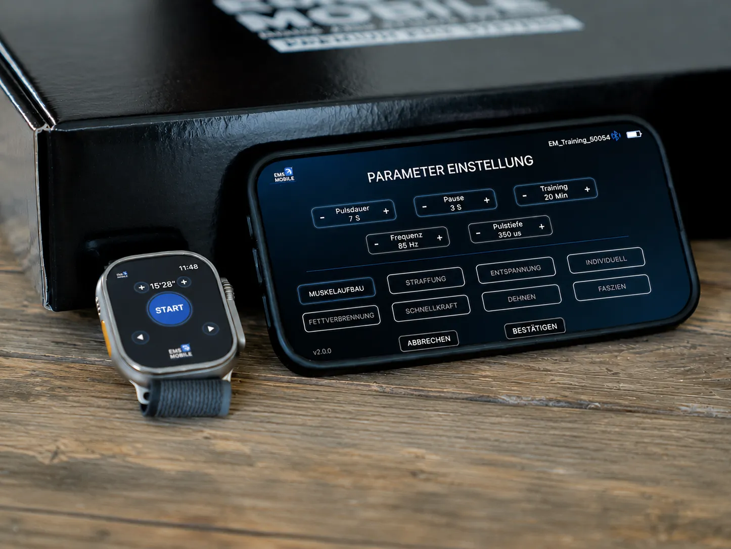 Apple Watch mit Start-Button und iPhone querformat mit der HOME-EMS-Steuerung — daneben die EMS-Mobile-Box auf Holzuntergrund.
